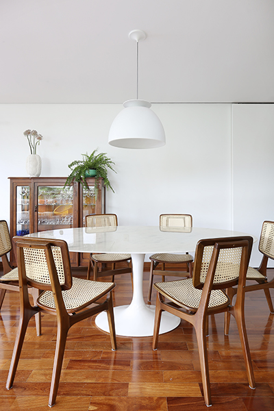 sala de jantar a mesa Sarinen branca, cadeiras em madeira e palhinha e luminária Bossa também na cor branca
